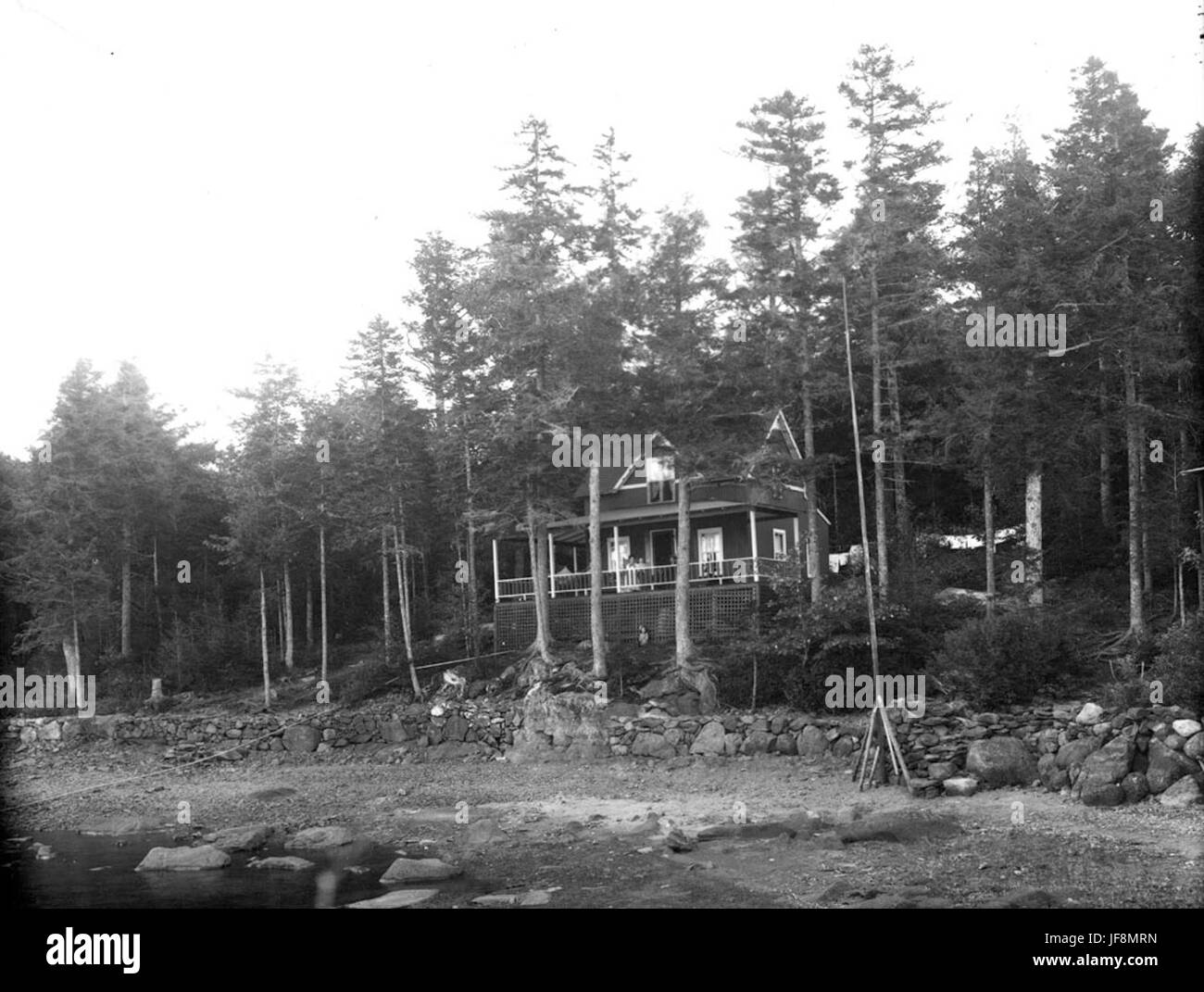 Ein historisches Bild eines Hauses mit Blick auf einen steinigen Strand, aufgenommen in einer Vintage-Illustration. Die Szene zeigt eine friedliche Lage am See mit natürlichen Felsformationen und ruhigen Gewässern. Stockfoto