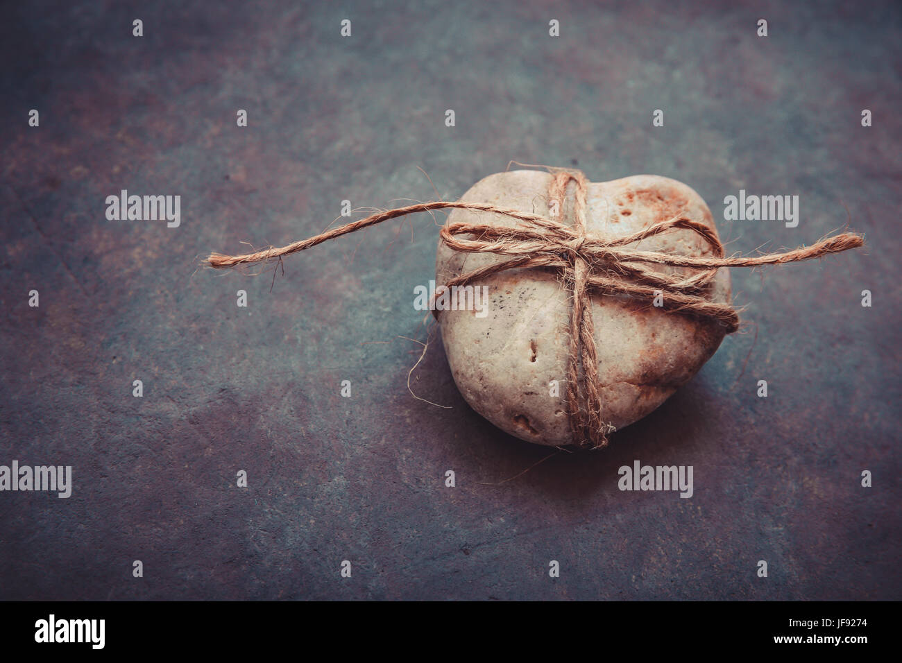 Herzförmige Felsen Kieselstein gebunden mit Bindfaden auf lila Stein dunkelblauem, konzeptionelle, Beziehung, Valentine, Ehe, Scheidung, abstrakte Stockfoto