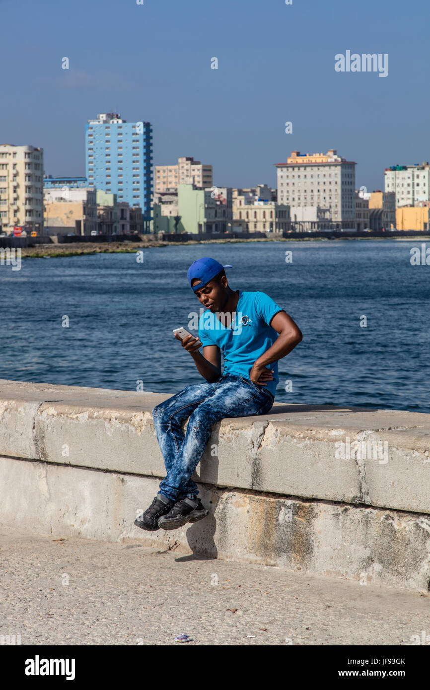 Junger kubanischen Mann nutzt sein Handy sitzt auf dem MALECON - Havanna, Kuba Stockfoto