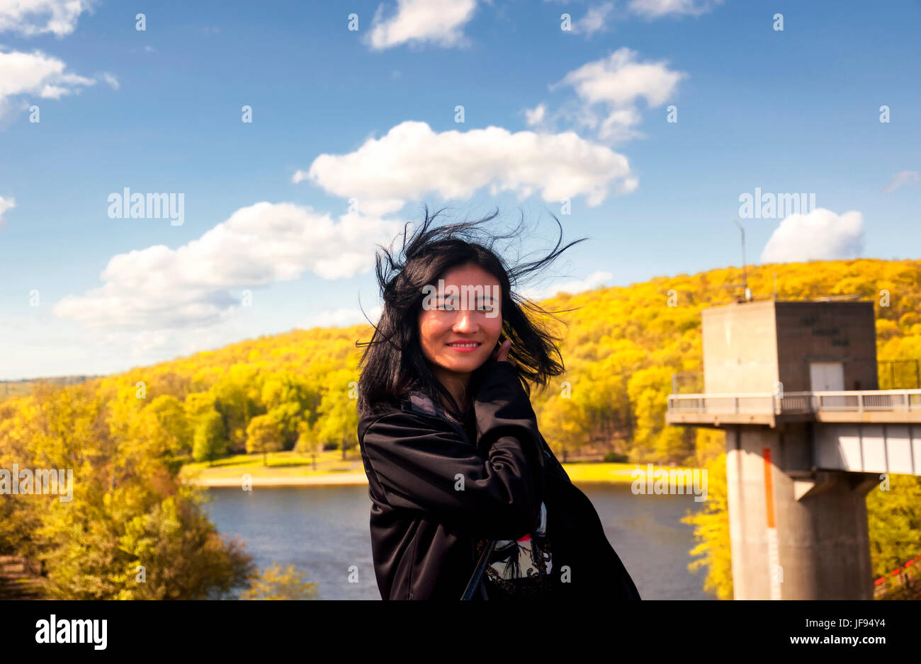 Eine Chinesin mit ihrem Haar wehen außer Kontrolle auf der Seeseite der Hop Brook Dam in Naugatuck Connecticut an einem sonnigen blauen Himmel Tag. Stockfoto