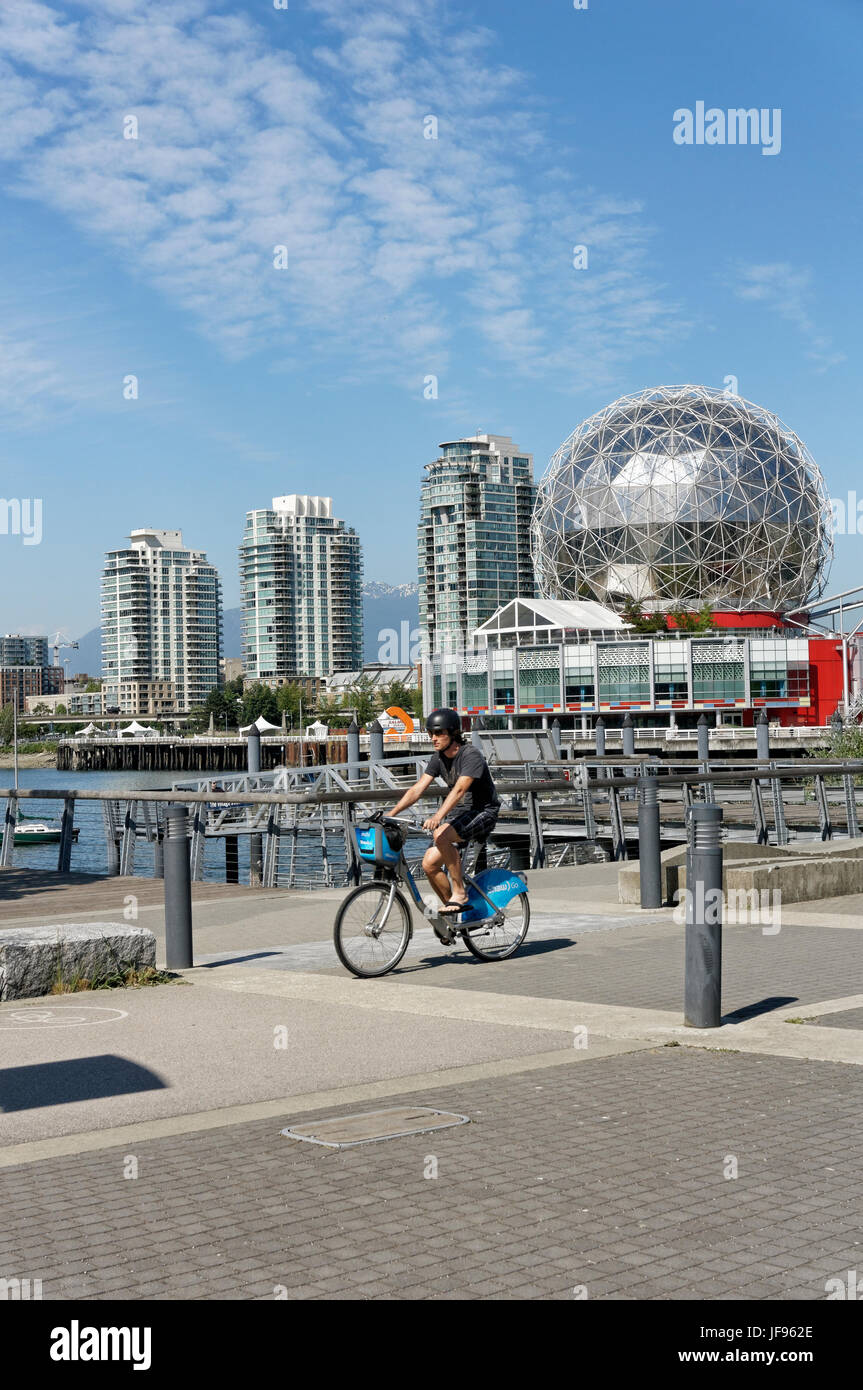 Mann reitet Mobi Bike-sharing-Fahrrad mit TELUS World of Science Dome auf der Rückseite in das Dorf am False Creek, Vancouver, Britisch-Kolumbien, Kanada Stockfoto