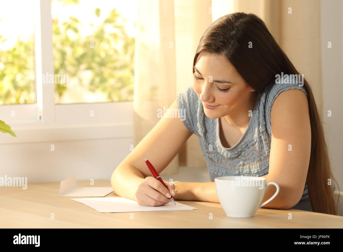 Glückliches Mädchen schreibt einen Brief an einen Tisch zu Hause Stockfoto