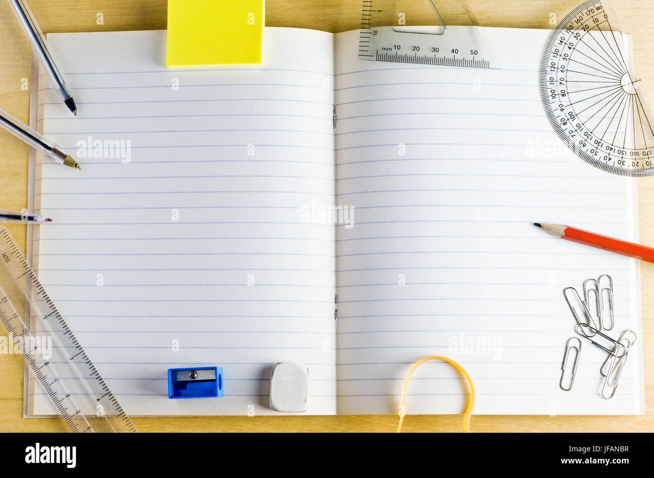Overhead Schuss von einem geöffneten Schulheft. umgeben von Schreibwaren auf einem leichten Holz Schreibtisch. Gefütterte Seiten bieten Textfreiraum. Stockfoto