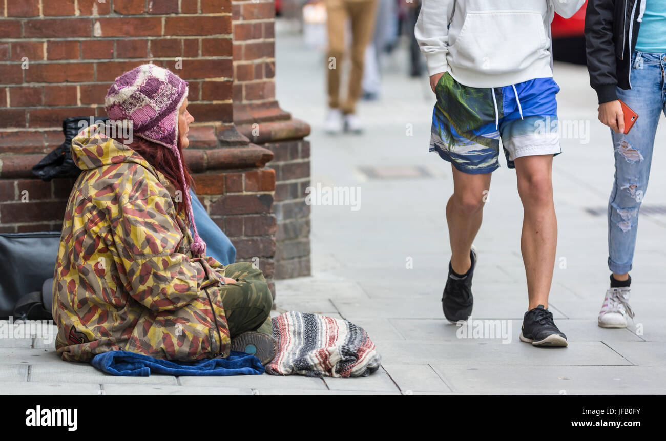 Obdachlose Dame sitzt auf dem Boden wie Menschen ignorieren sie vorbeigehen. Stockfoto