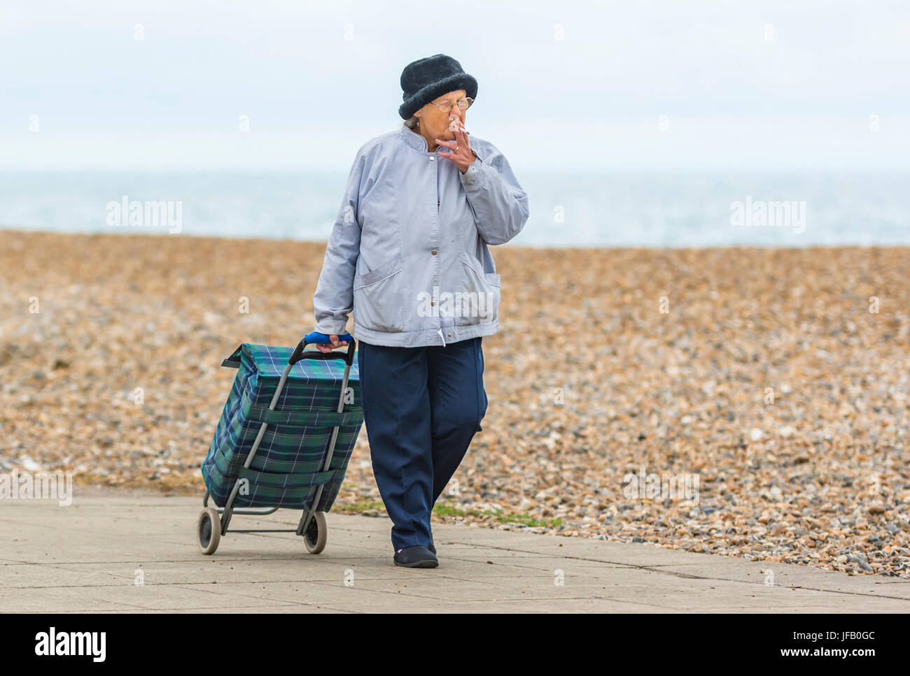 Ältere Dame, die beim Rauchen einen Einkaufswagen zieht, in Großbritannien. Stockfoto