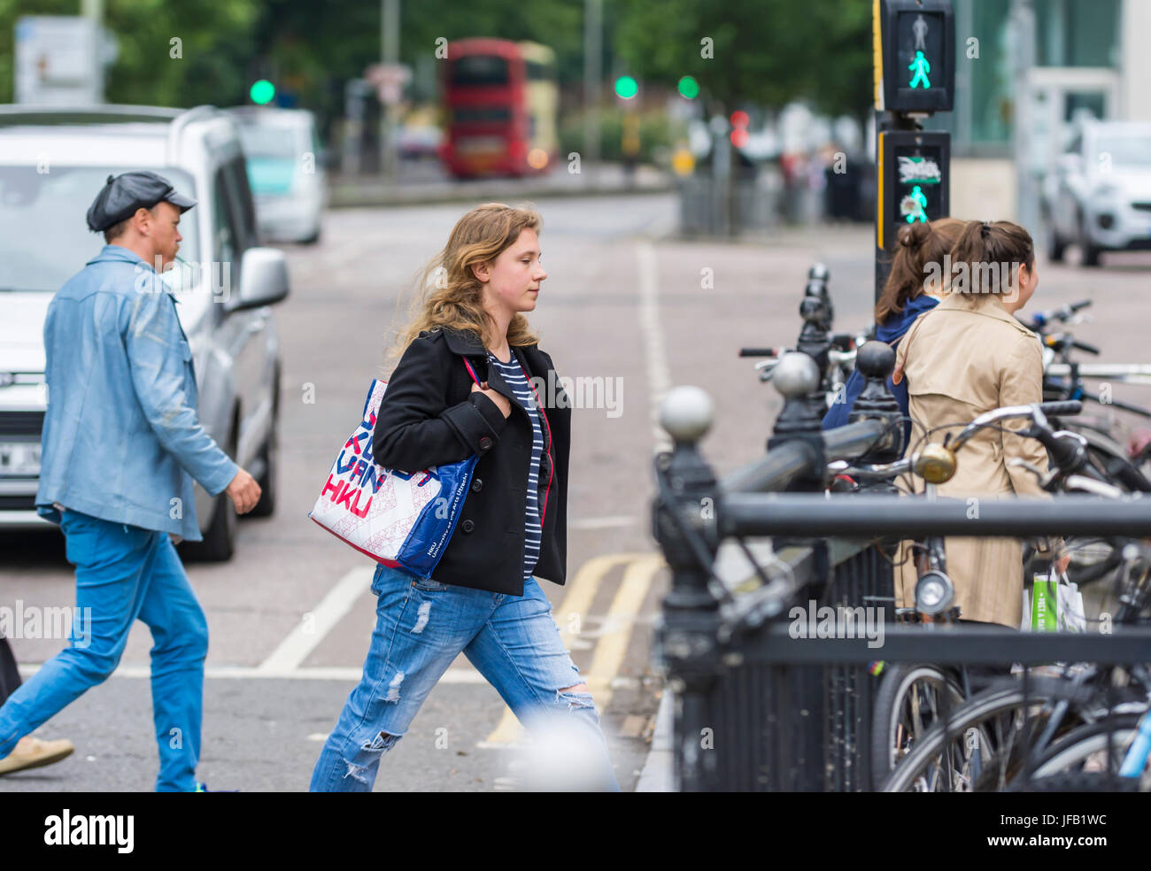 Frau überqueren einer Straße in einer Stadt, leuchtet der grüne Mann an einem Fußgängerüberweg im Vereinigten Königreich. Stockfoto
