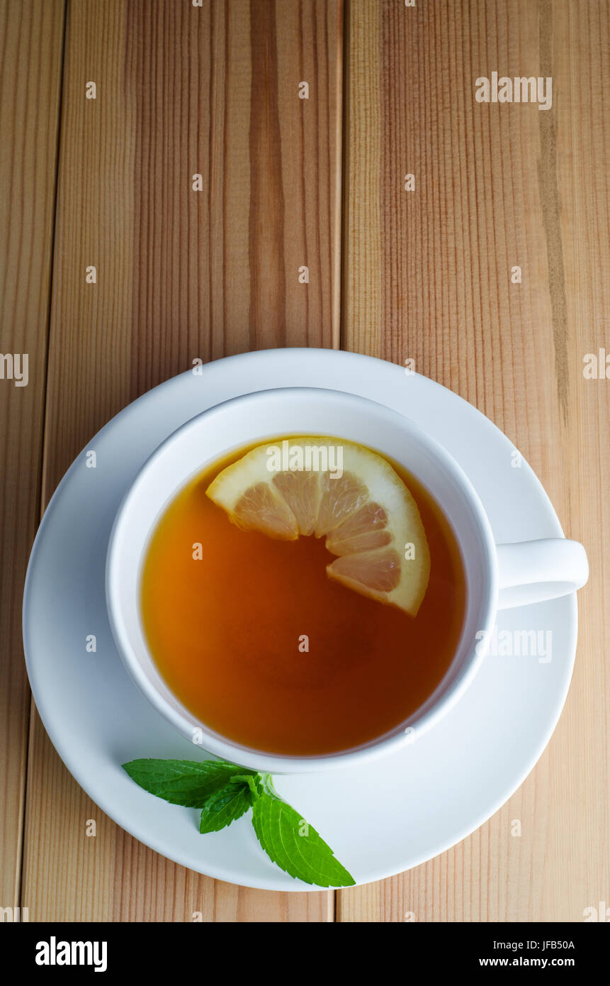Overhead Schuss Zitrone Tee in eine weiße Tasse mit Untertasse mit halben Zitronenscheibe und Minze Blätter auf einem Holztisch geplankte. Stockfoto