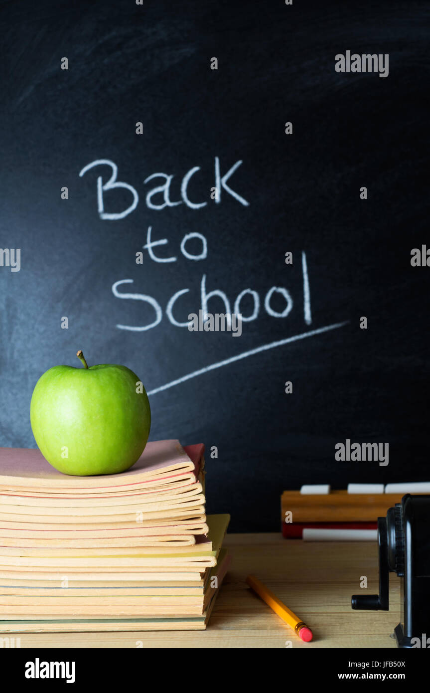 Lehrerpult mit einem Stapel von Büchern, einen Apfel und andere Geräte.  Die Worte "Back to School", geschrieben mit Kreide an die Tafel in soft-Fokus backgr Stockfoto