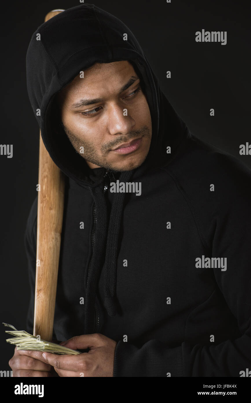 junger Räuber im Zoodie mit Baseballschläger und Geld isoliert auf schwarz Stockfoto