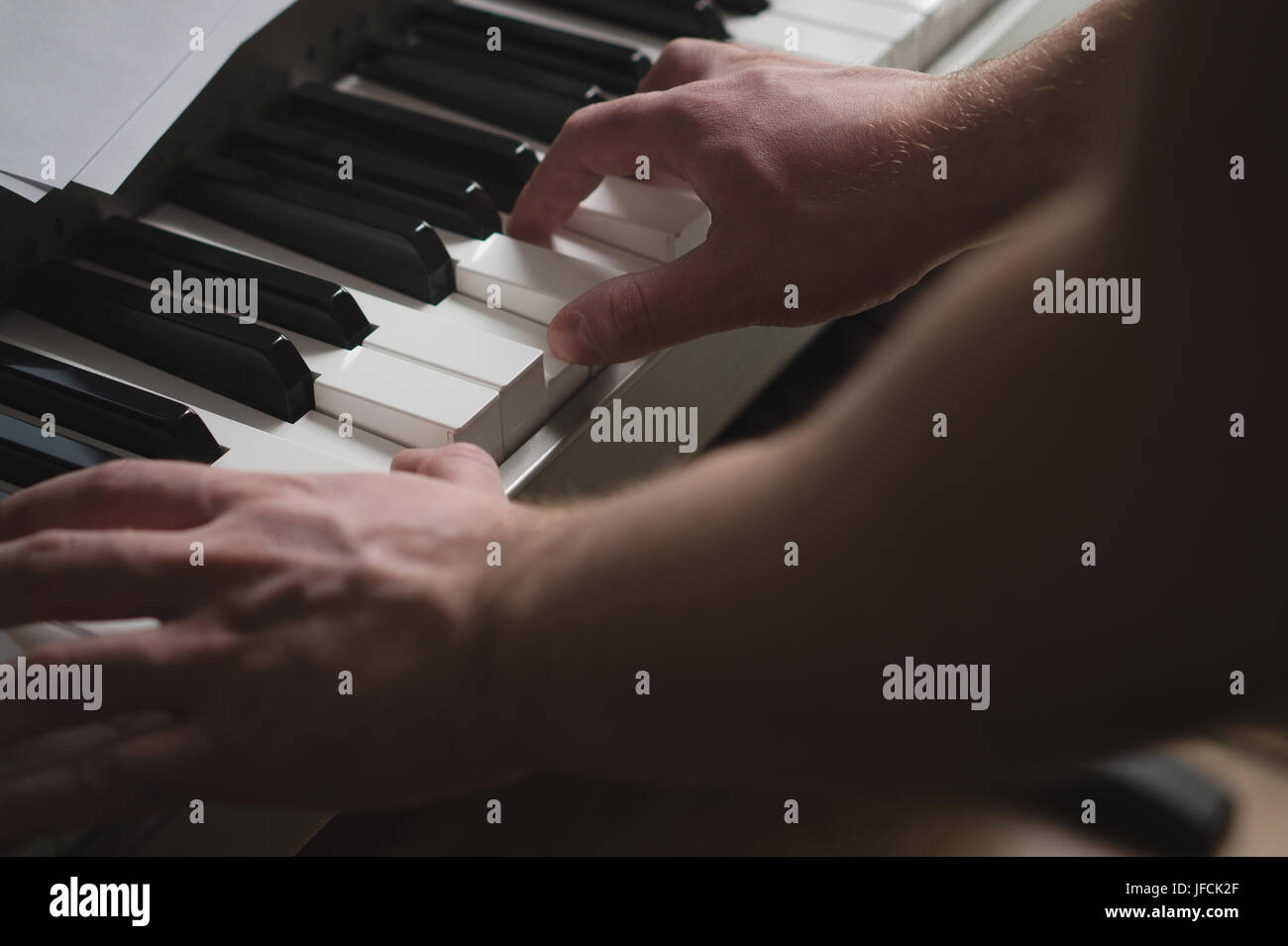 Nahaufnahme von Mann Klavier zu spielen. Intimer Blick auf Hände auf Tasten der Tastatur. Filmische und dramatische Atmosphäre und Ambiente-Beleuchtung. Talentierter Pianist. Stockfoto