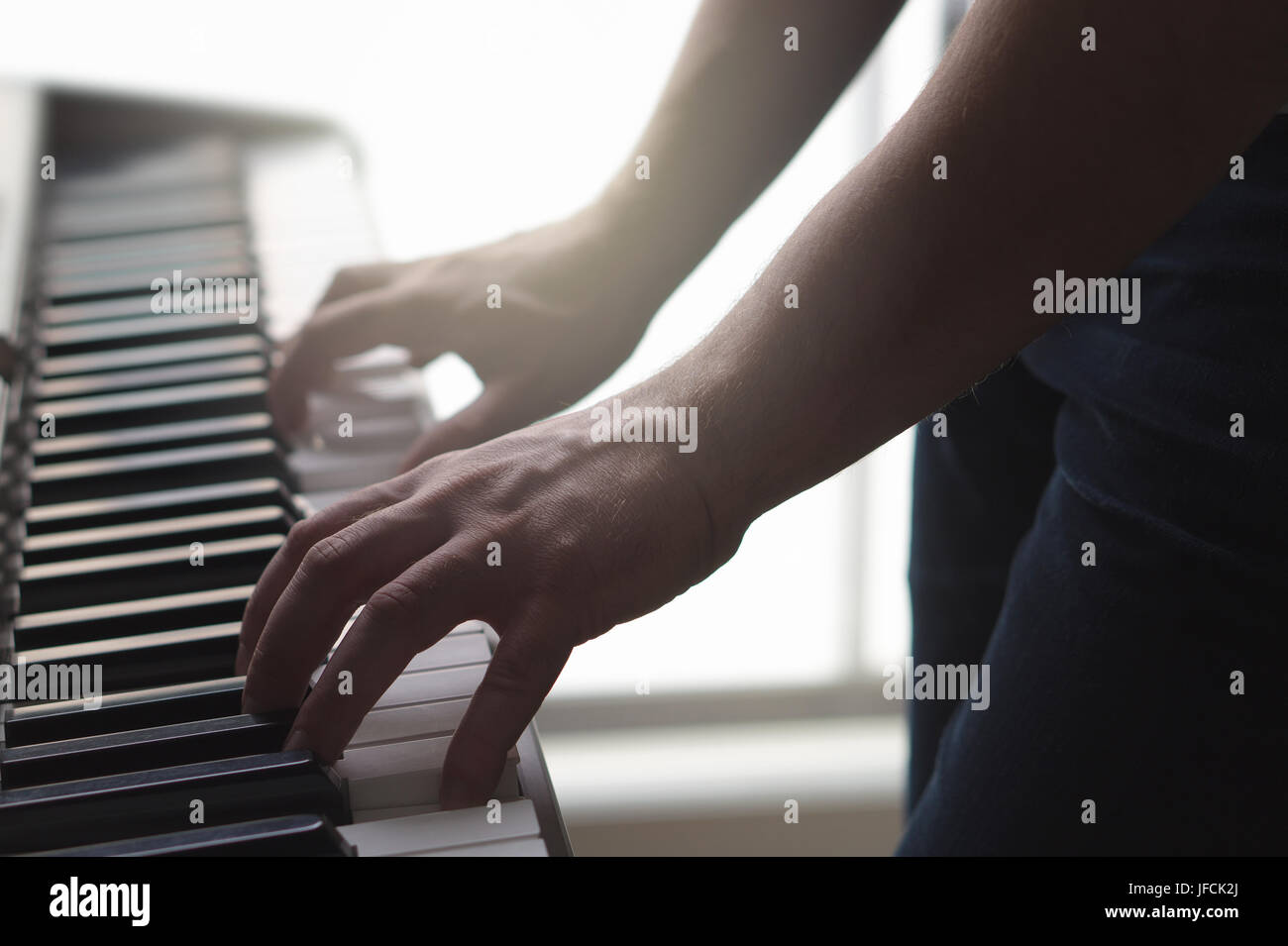 Mann, spielt Klavier stehen im Heimstudio. Ambient Stimmung mit Sonnenlicht. Nahaufnahme von männlichen Händen auf Tasten elektronische Tastatur. Person spielt Musik. Stockfoto