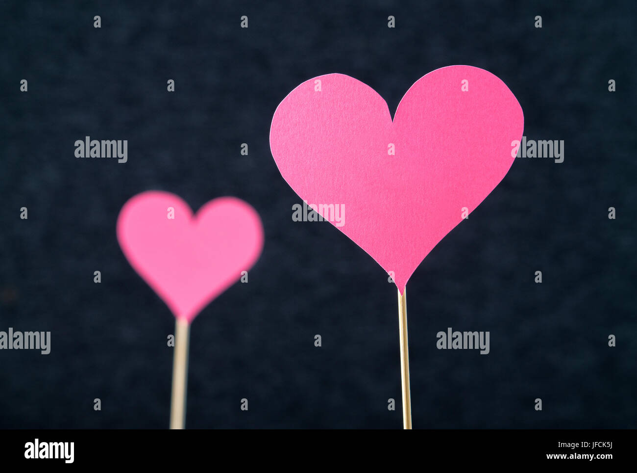 Zwei romantische Herzen schneiden Sie aus Pappe oder Papier auf Holzstab und dunklen Hintergrund. Schöne, handgefertigte rosa rote Liebe Formen. Stockfoto