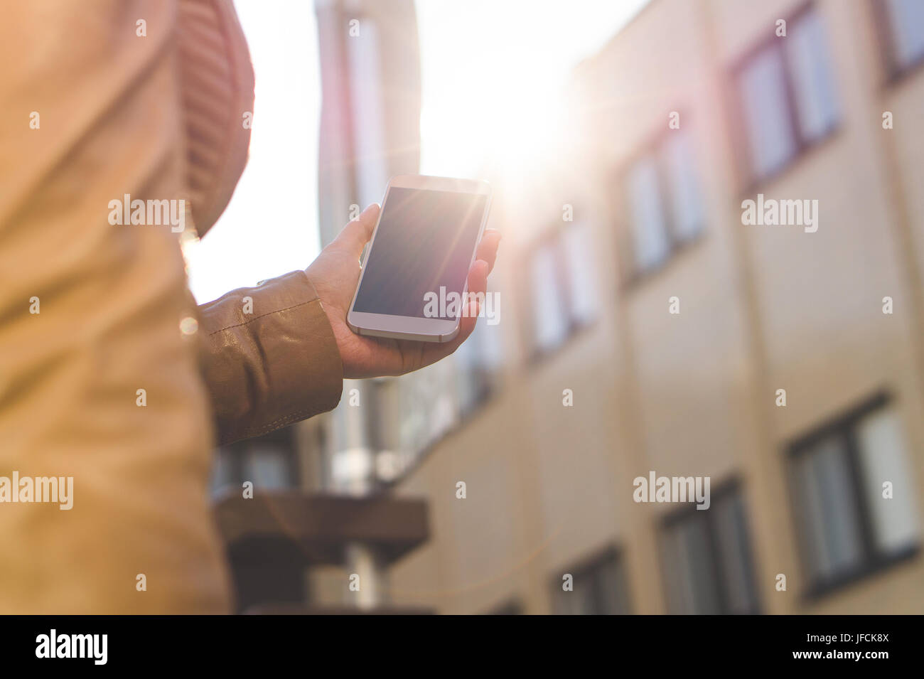 Junge Frau zu Fuß mit Smartphone in der Sonne. Nahaufnahme von Mädchen hält Handy in der hand. Morgens oder abends Fuß in die Stadt. Lebensstil Stockfoto