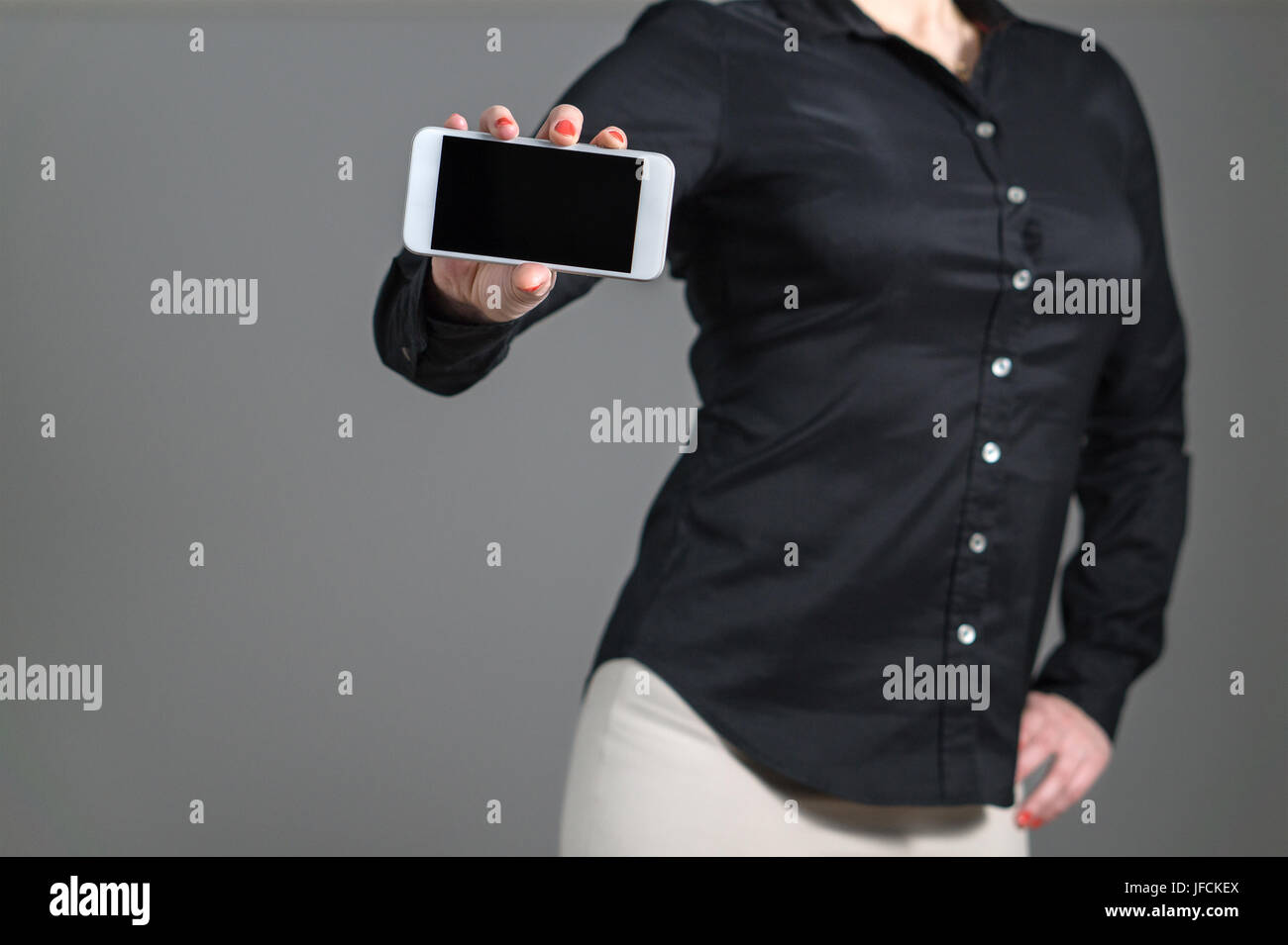 Business-Frau präsentieren eine mobile Anwendung oder ein Foto. Mädchen halten Smartphone mit dynamischen Pose und schwarzen Hemd mit Kragen. Leerer Bildschirm. Stockfoto