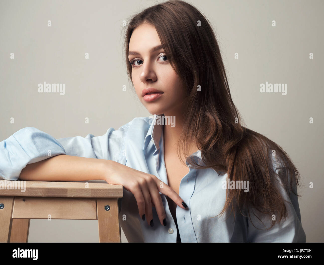 Schöne junge Frau trägt blaue Herrenshirt. Modell auf hölzernen Schemel sitzt. Stockfoto