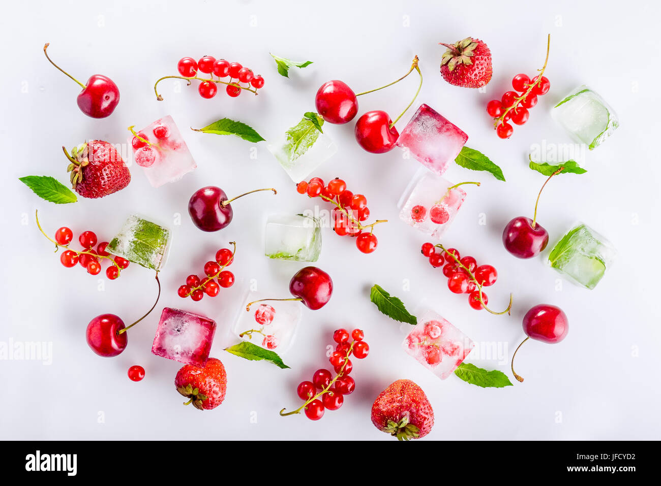 Draufsicht auf Eiswürfel mit frischen Beeren unter nicht gefrorene Kirschen, Erdbeeren und Minze Blätter auf dem weißen Hintergrund. Selektiven Fokus Stockfoto