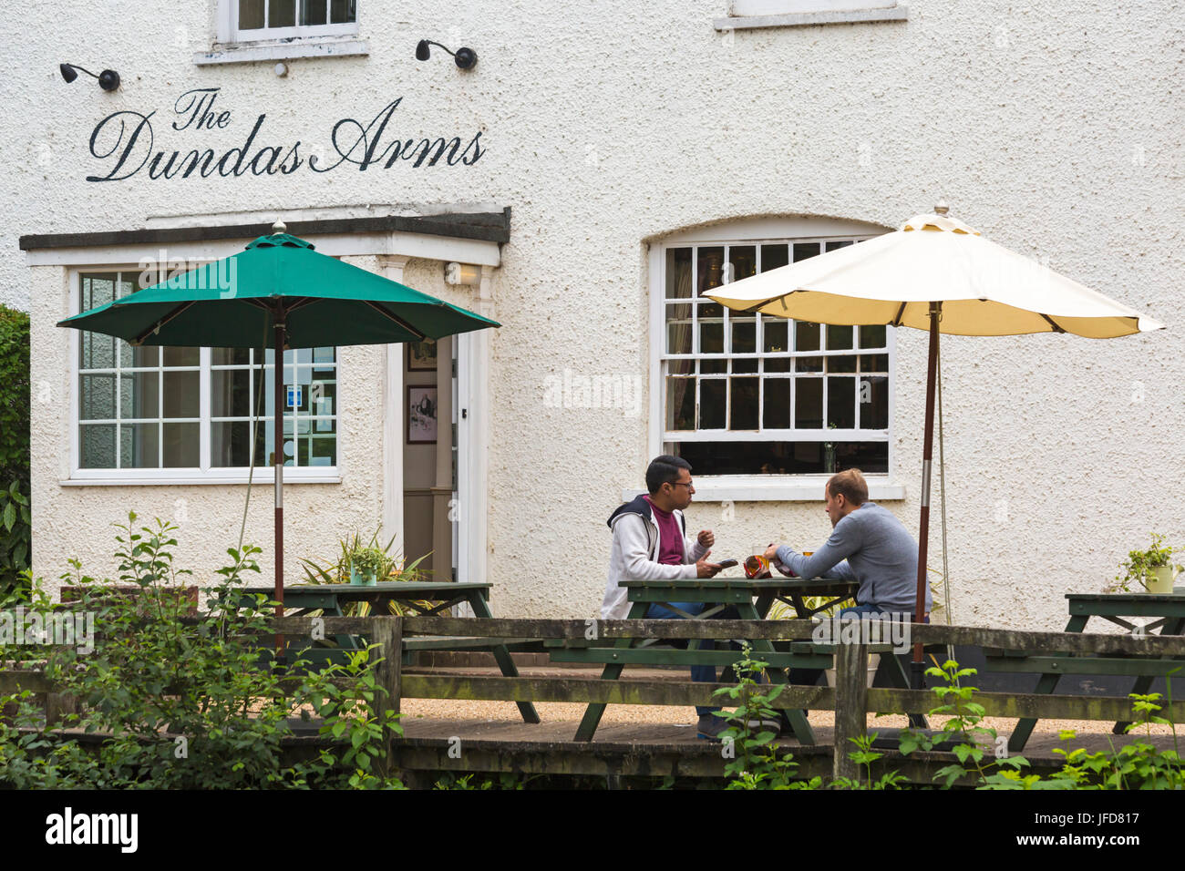 Zwei junge Männer, die im Juni vor dem Dundas Arms Pub in Kintbury, West Berkshire, Großbritannien, etwas zu essen und zu trinken haben Stockfoto