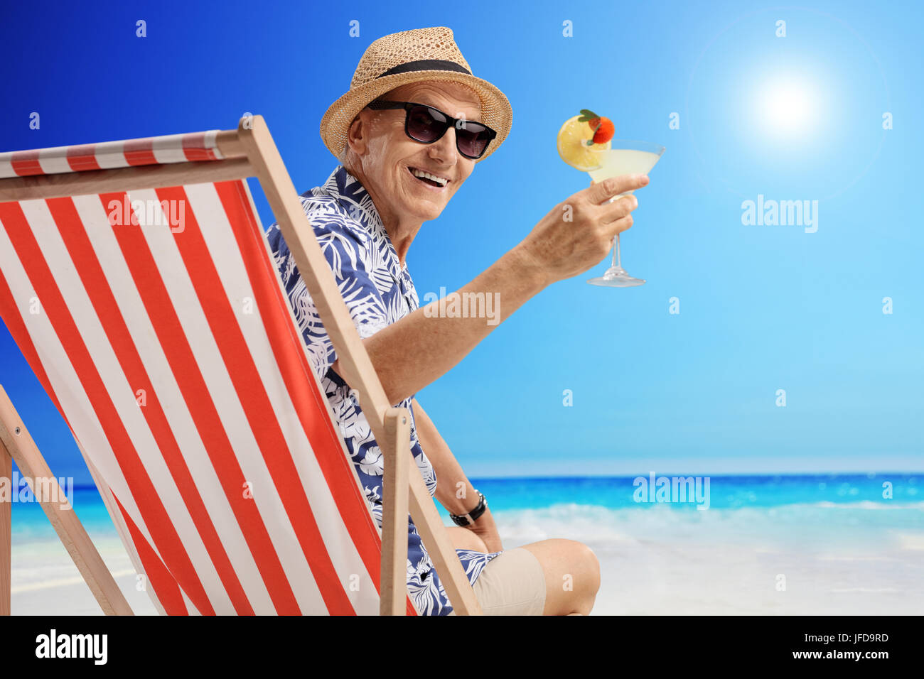 Reifer Mann mit einem cocktail sitzt in einem Liegestuhl am Strand Stockfoto