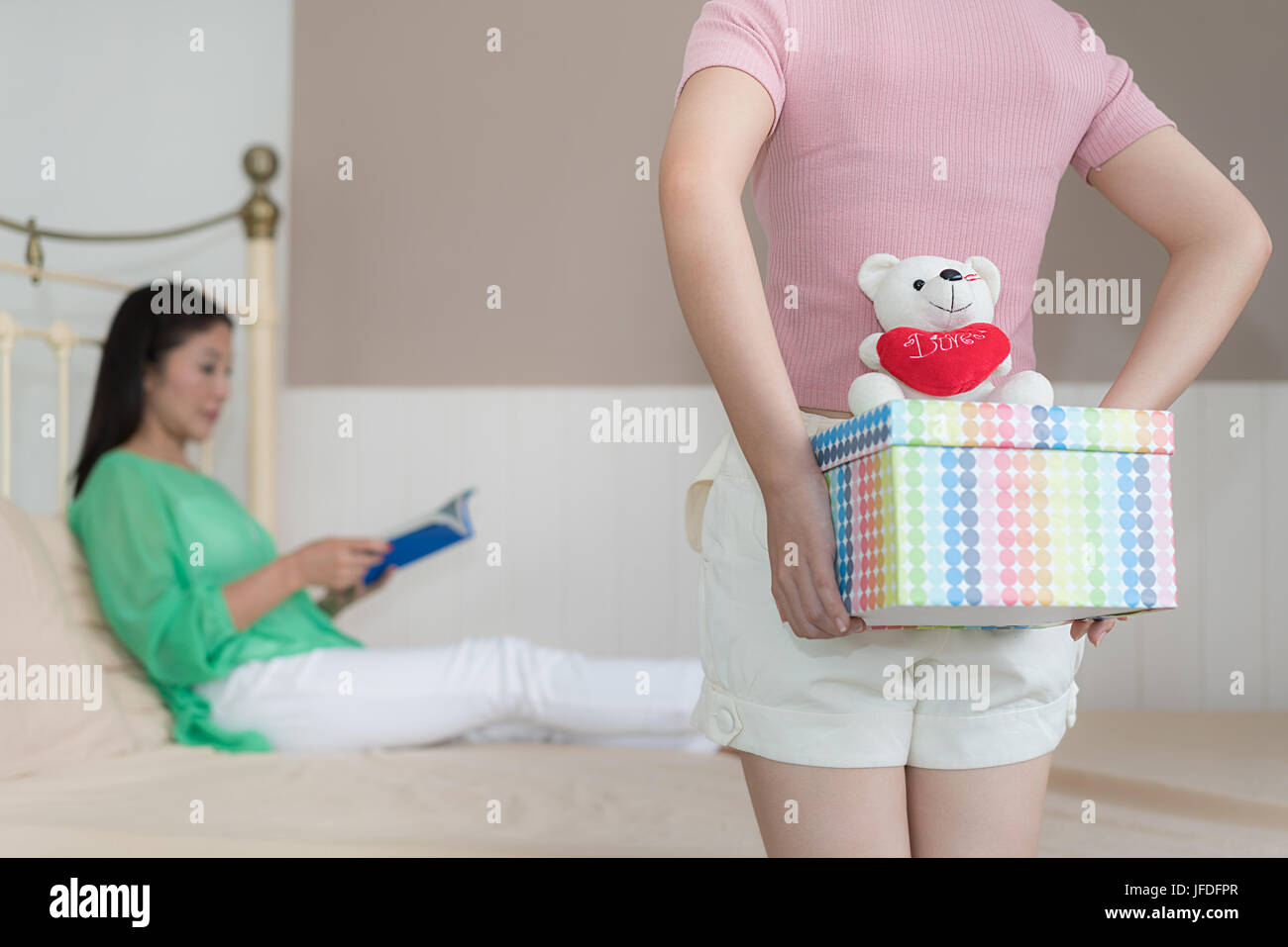 Asiatische Teenager Tochter versteckt Geschenkbox von Mutter sitzt auf dem Bett zu Hause. Stockfoto