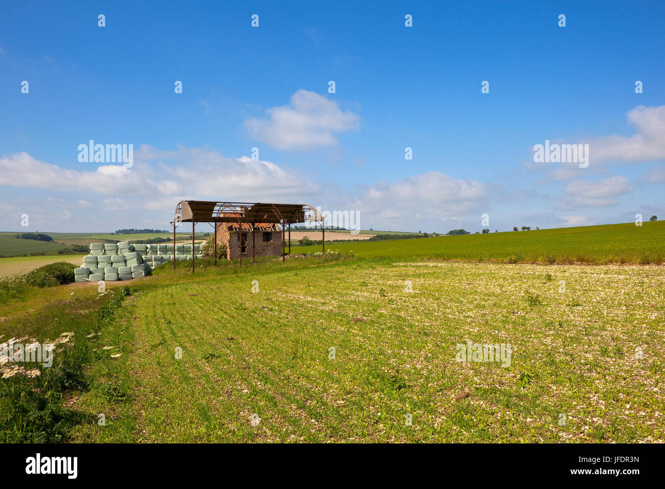 ein Alter Hof mit Kunststoff gewickelten Ballen in der Nähe einer Scheune auf einem Hügel in der Yorkshire Wolds unter einem blauen Sommerhimmel Stockfoto