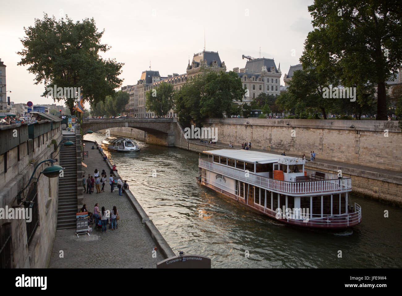 Boote fahren entlang der Seine und Parisern sitzen entlang den Ufern des Flusses. Stockfoto