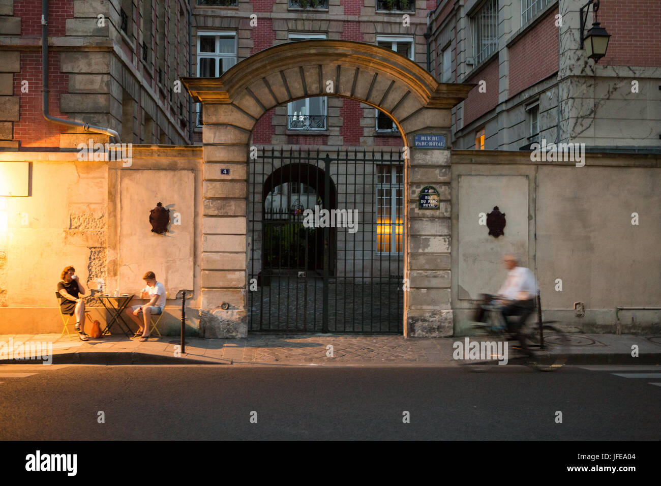 In der Abenddämmerung isst ein paar im Freien in einem Restaurant, während ein Mann reitet auf seinem Fahrrad. Stockfoto