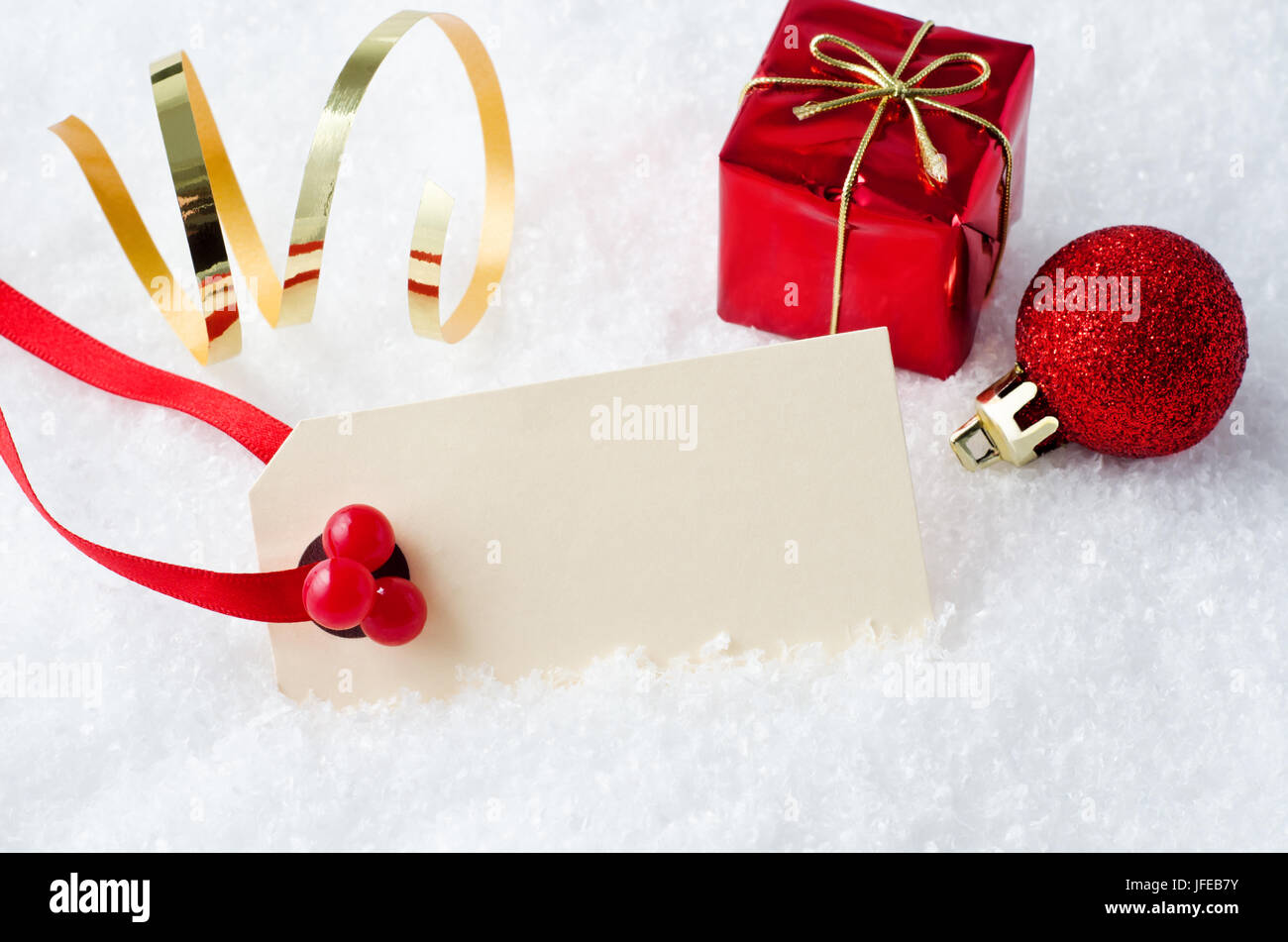 Eine leere Creme farbige Weihnachten Tag am roten Band mit künstlichen Stechpalme Beeren, teilweise eingetaucht in Dekoschnee mit Goldfolie Twist, Geschenk-Box und Stockfoto