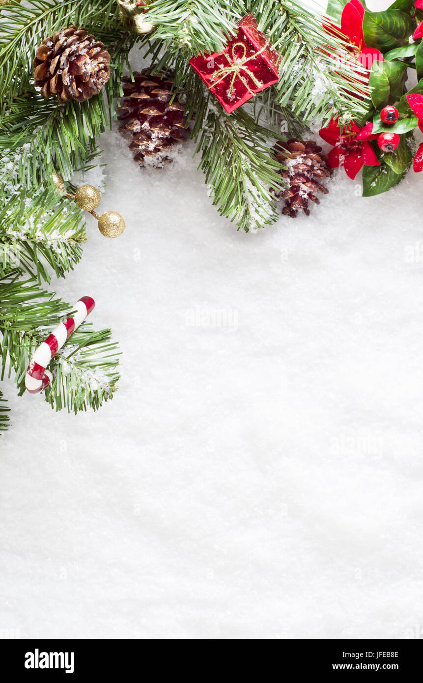 Eine Weihnachten Grenze nach links und von oben des Rahmens aus künstlichen Laub, echte Tannenzapfen und dekorative Ornments, bestreut mit Schnee auf einem gefälschten s Stockfoto