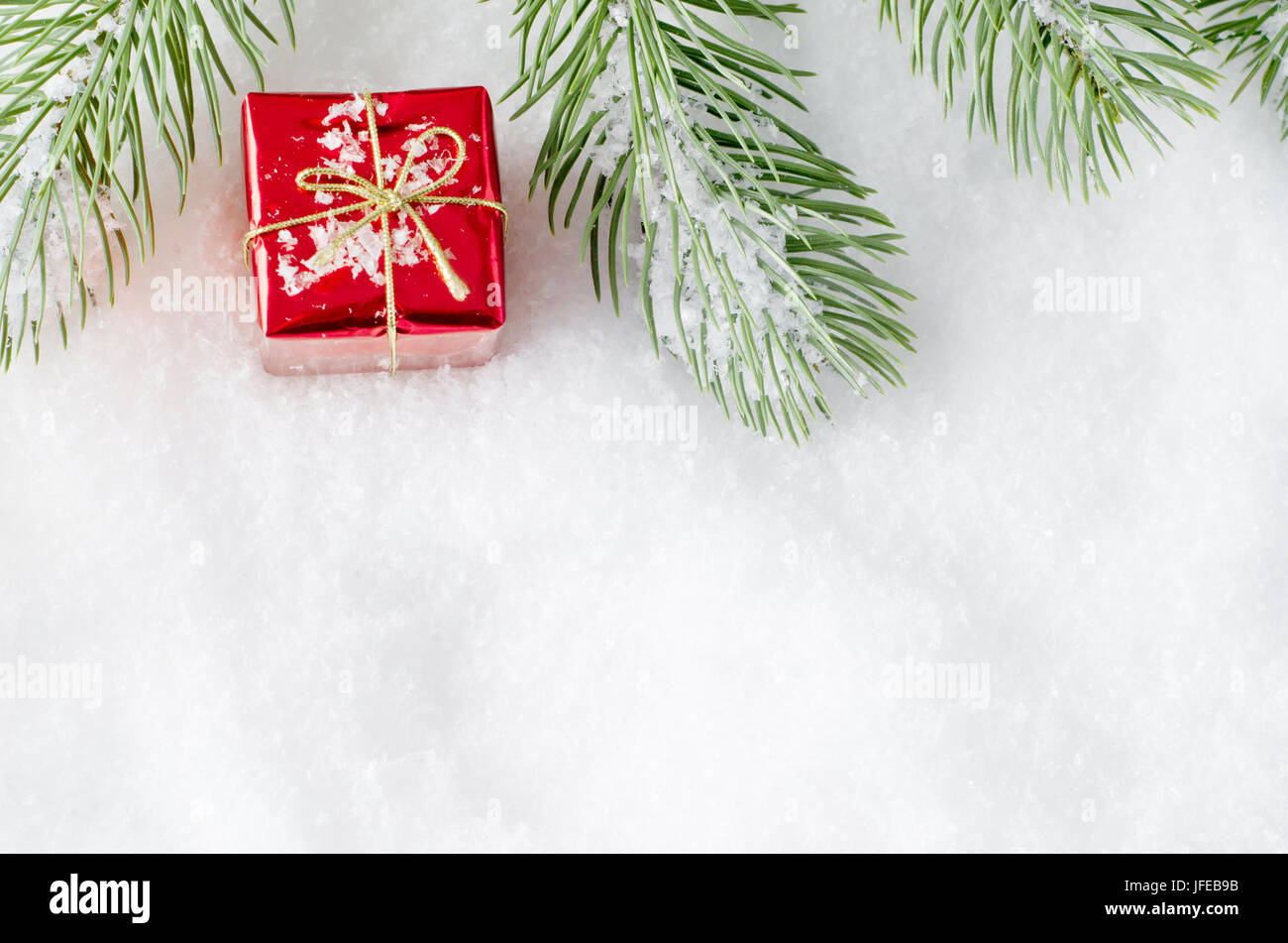 Ein oberen Rahmen Weihnachten Grenze des künstlichen Baum Wedel auf Kunstschnee mit kleinen glänzenden roten Geschenk-Box zwischen gelegt. Stockfoto