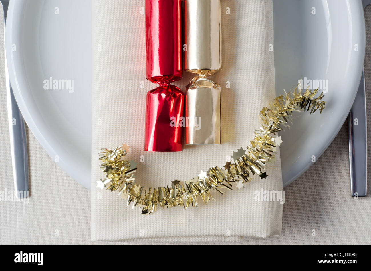 Overhead Schuss, Weihnachtsessen, mit roten und goldenen Cracker und Lametta gelegt auf einer Serviette, Teller, Besteck und Tischdecken unter darstellt. Stockfoto