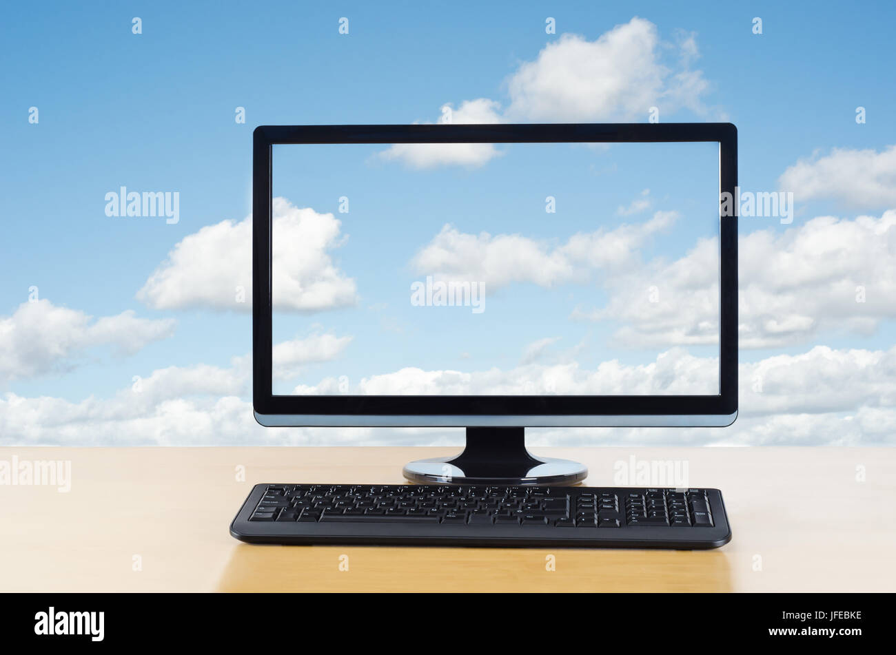 Konzeptbild von Cloud computing.  Computer-Monitor und Tastatur auf Holz Leuchttisch mit Blick auf den Betrachter vor flauschige weiße Wolken auf blauem Stockfoto