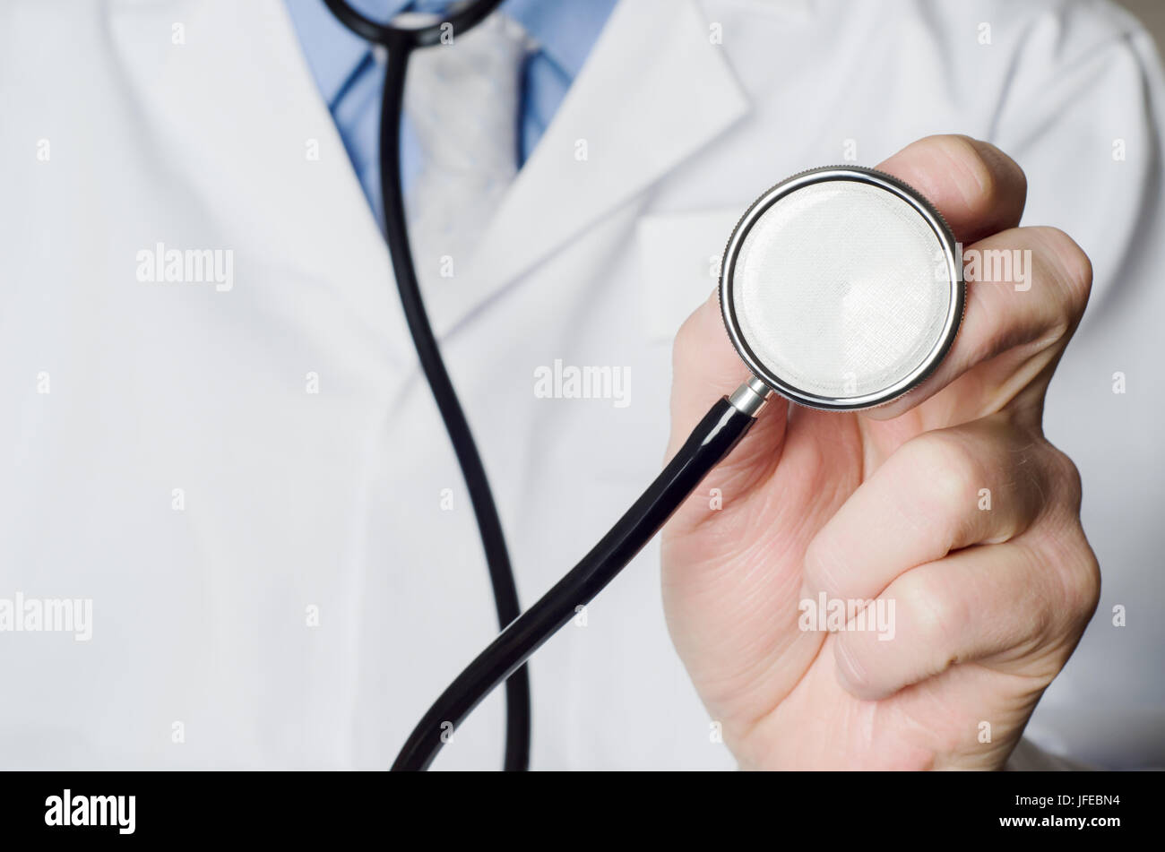 Nahaufnahme eines Arztes Hand, halten ein Stethoskop ausgestreckt auf den Betrachter.  Weißen Arztkittel Eingabefeld auf der linken Seite des Rahmens. Stockfoto