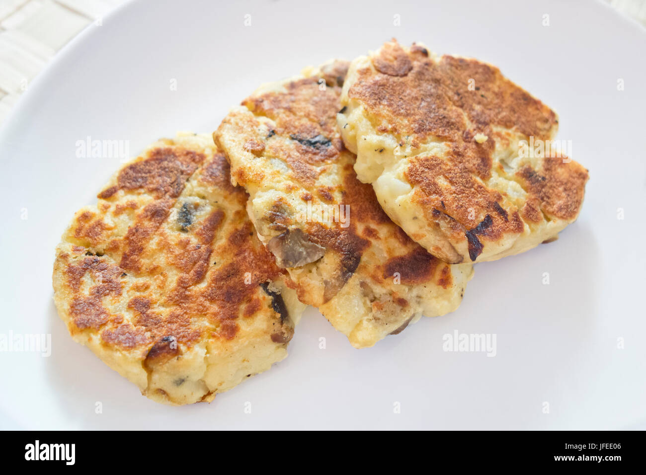 Kartoffelkuchen mit Pilzen auf einem weißen Teller. Kartoffelpuffer, ein Snack auf pflanzlicher Basis. Stockfoto