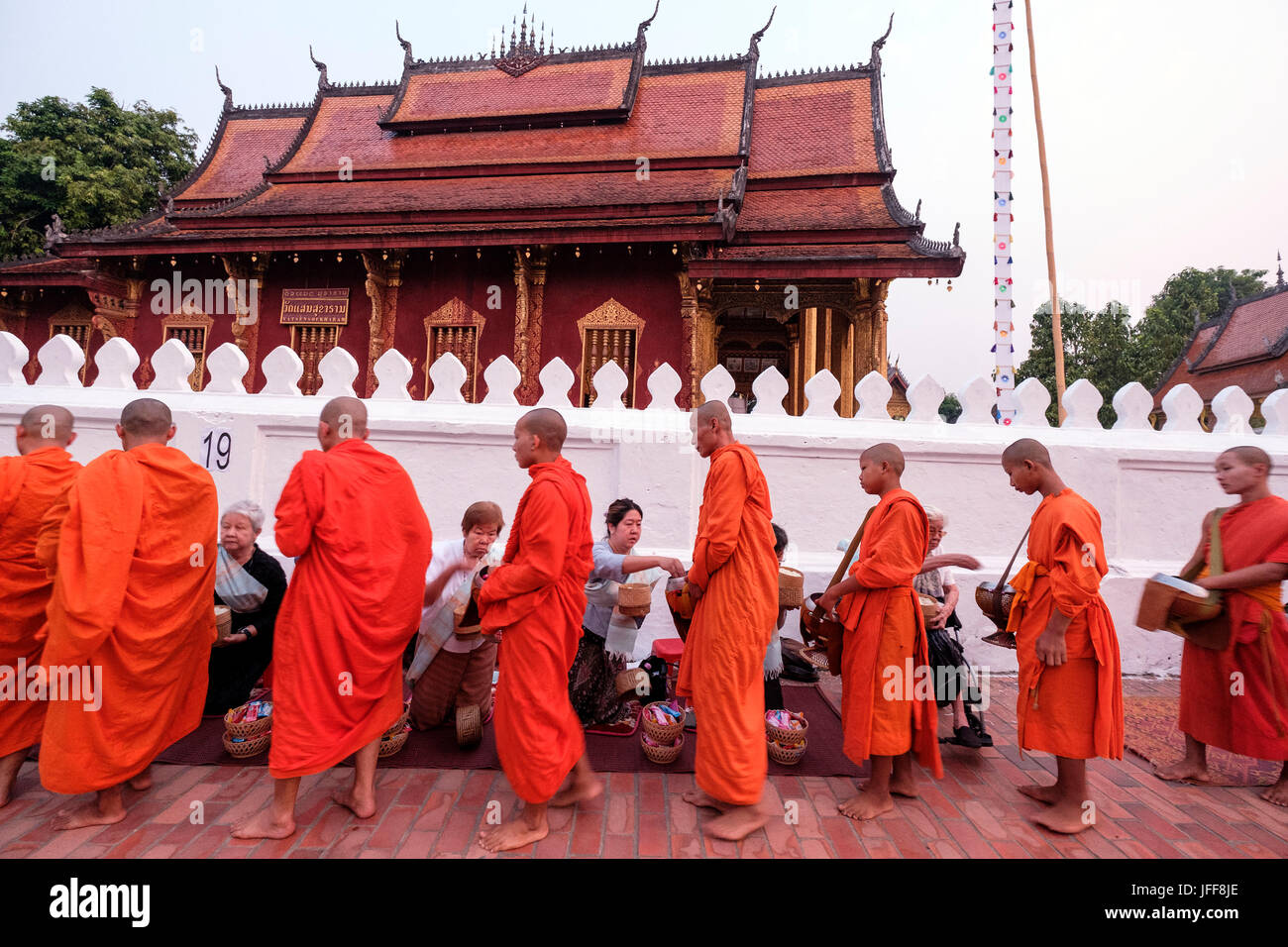 Buddhistische Mönche tragen orangefarbene Gewänder Spaziergang durch den Tempel Wat Sensoukaram Geschenke auf den Straßen von Luang Prabang, Laos, Asien zu sammeln Stockfoto