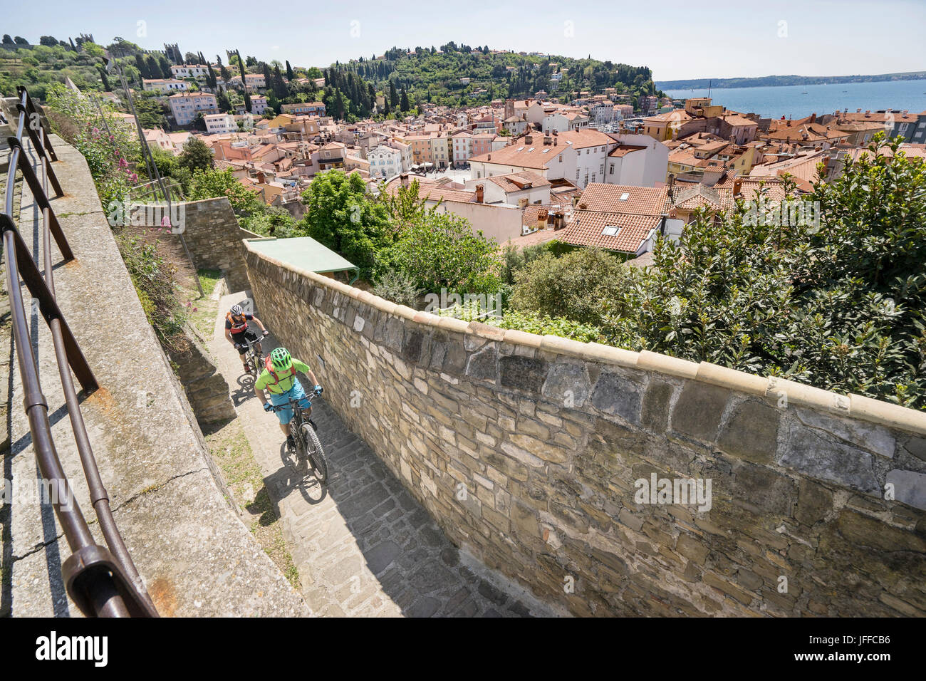 Biker, klettert auf gepflasterten Fläche von Steinmauer mit Häusern im Hintergrund Stockfoto