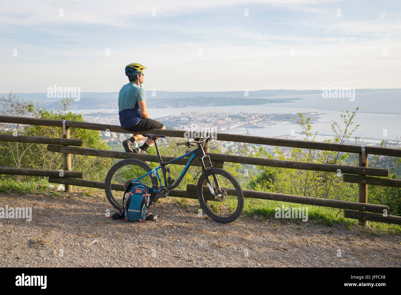 Mountainbiker, die sitzen auf Holzgeländer und Blick auf See und Stadt Stockfoto