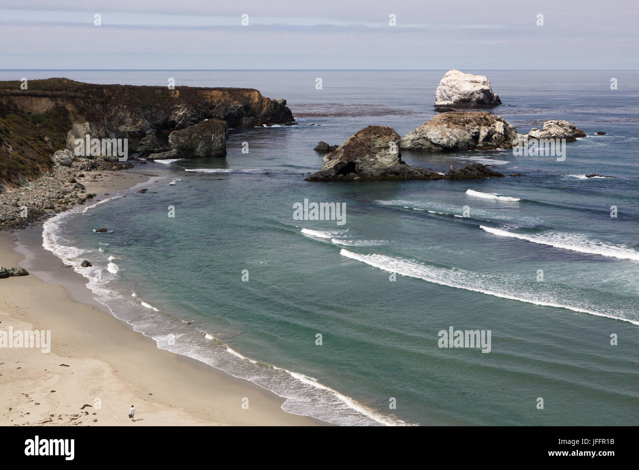 Wellen kommen an Land an der Big Sur Küste. Eine einsame Person Spaziergänge am Sandstrand. Stockfoto
