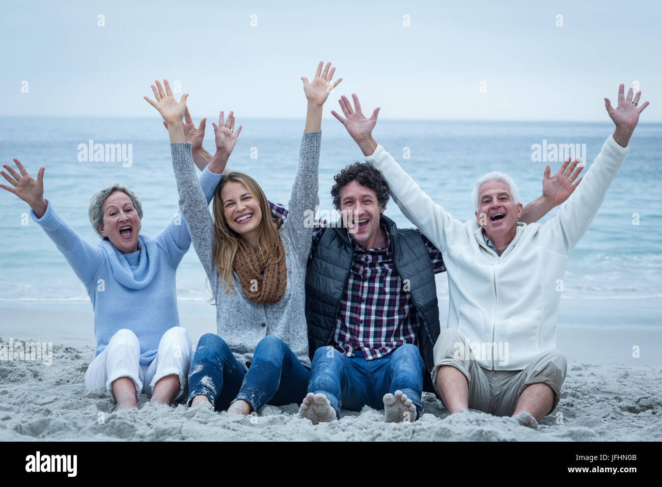 Familie mit erhobenen Armen sitzen im Sea Shore Stockfoto