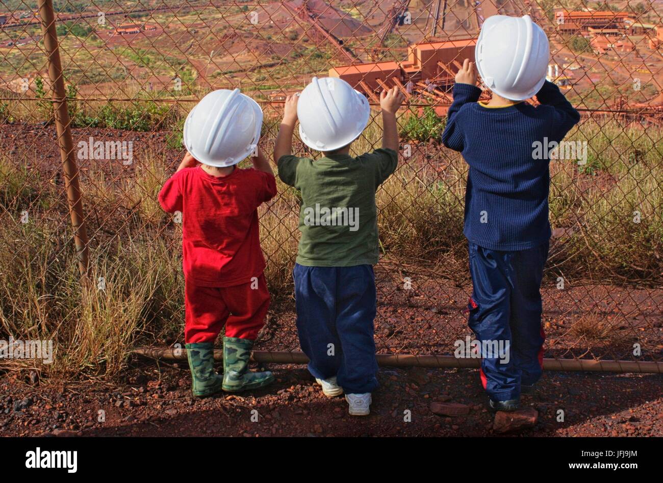 Drei Kinder mit schützenden Bergbau Helmen Blick durch ein Maschendrahtzaun an der Mount Tom Preis mir, WA, Australia. Stockfoto