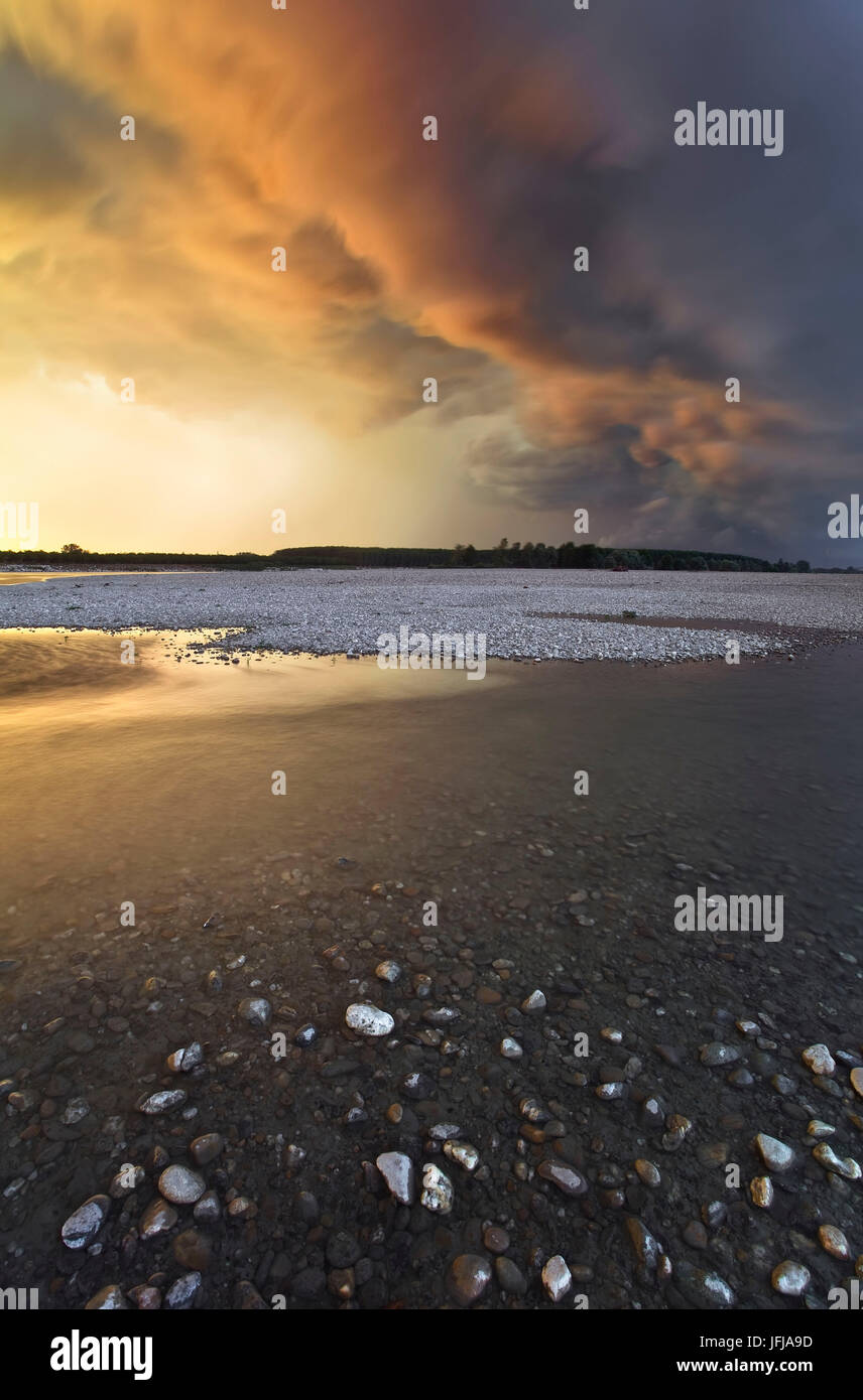 Po River Park, Piemont, Italien, felsigen Strand am Po-Ufer, mit stürmischen Wolken durch den Sonnenuntergang Lichter gefärbt, Stockfoto