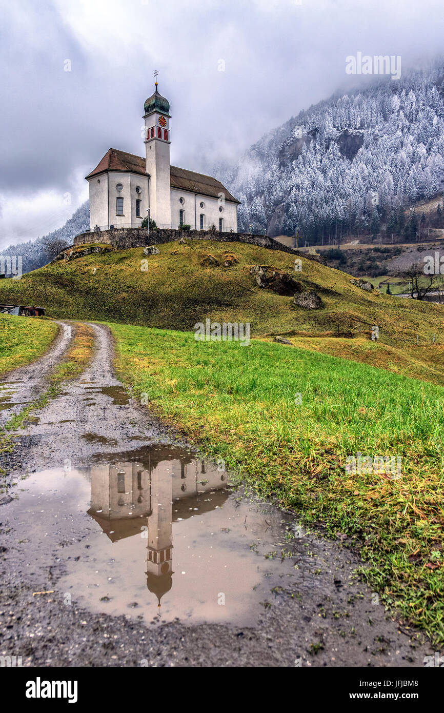 Die Kirche von Wassen spiegelt sich in einer Pfütze nach einem Winter Schneefall, Andermatt, Kanton Uri, Schweiz, Europa Stockfoto