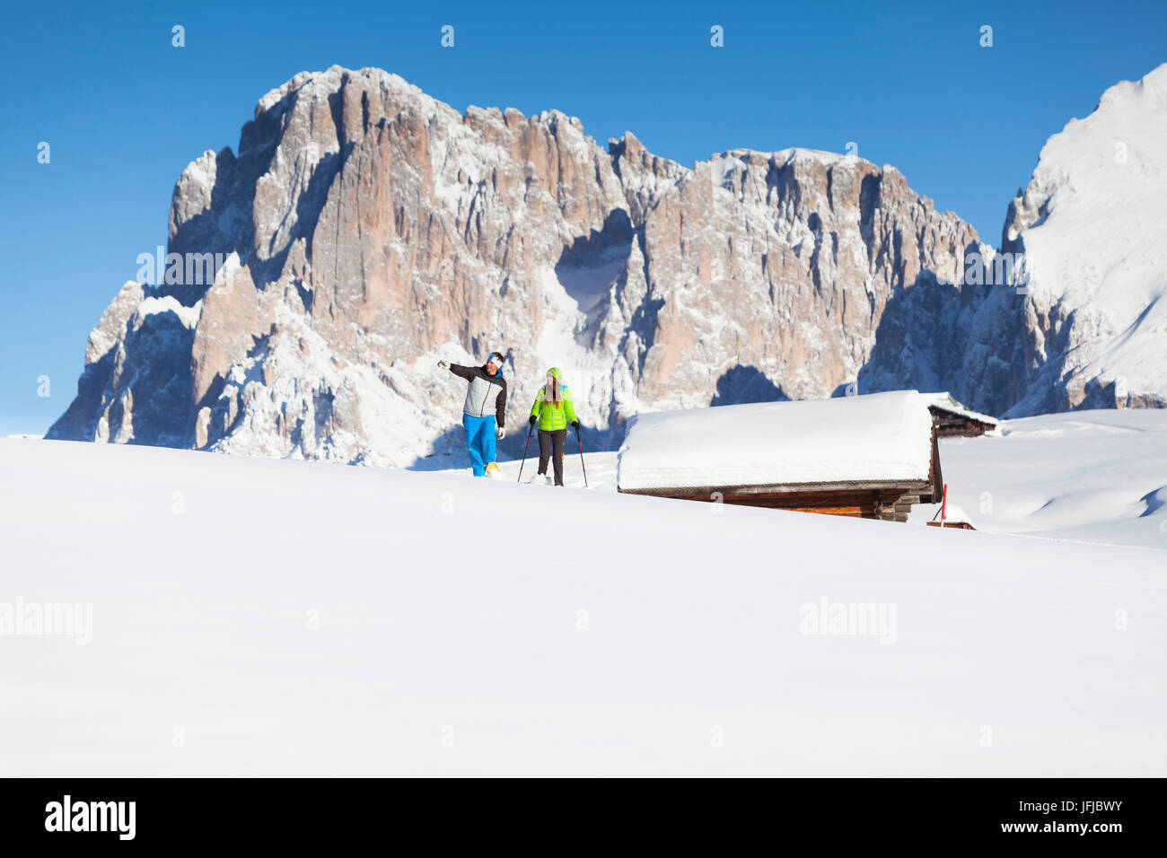 zwei Modelle sind in den frischen Schnee auf der Seiser Alm mit einigen Hütten und den Langkofel Peak im Hintergrund Bozen Provinz, Südtirol, Trentino Alto Adige, Italien, Europa Fuß Stockfoto