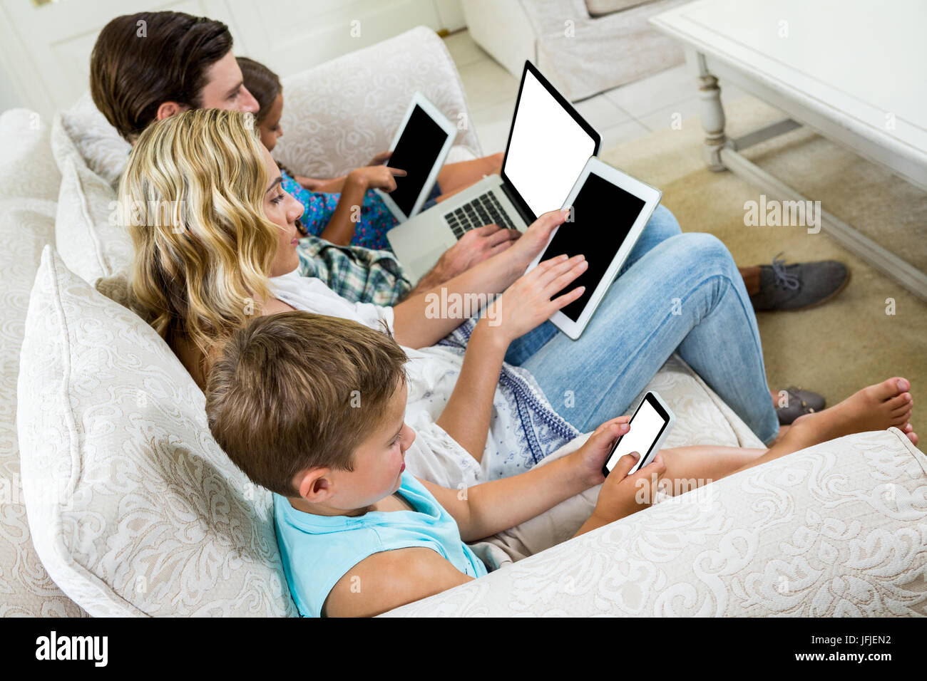 Familie mit verschiedenen Technologien sitzend auf sofa Stockfoto
