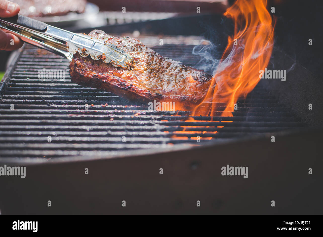 Steaks, das auf einem Grill kocht, mit Flammen, die um die Steaks heraufkommen. Stockfoto