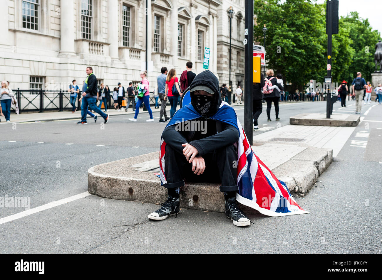 London, UK. 1. Juli 2017. LONDON, ENGLAND - 01. Juli Demonstrator mit schwarzer Kapuze und Maske sitzt in der Mitte von Whitehall mit dem Union Jack auf dem Rücken. Tausende von Demonstranten trat die Anti-Tory-Demonstration am 1. Juli 2017. Sie marschierten von der BBC Broadcasting House, Parliament Square. Sie forderten ein Ende der konservativen Regierung und Politik der Sparmaßnahmen. Bildnachweis: onebluelight.com/Alamy Live News Stockfoto