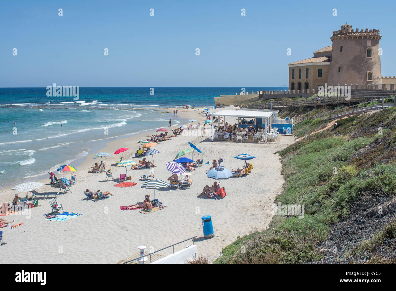 Sonnenanbeter am Strand mit den Schlossturm und die Strandbar am Torre De La Horadada in Alicante Spanien Stockfoto