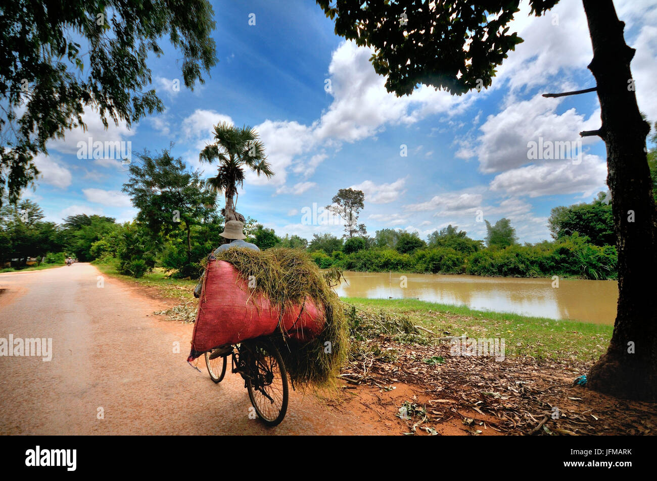 Ein Mann transportieren seine Ladung mit Fahrrad unter die weite Landschaft in ländlichen Dörfern entlang des Flusses, in der Nähe der See Tonle Sap, Siem Reap, Kambodscha Stockfoto