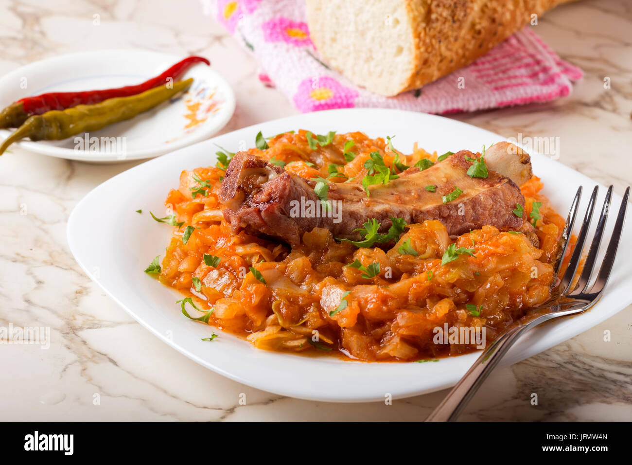 Kohl-Eintopf mit geräucherten Rippchen und grüner Petersilie serviert in weißen Teller mit eingelegtem Chili Paprika und Brot Stockfoto