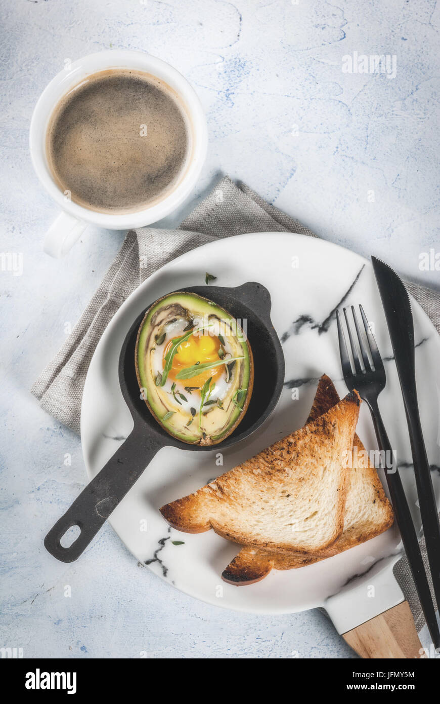 Gesunde vegane Frühstück. Ernährung. Gebackene Avocado mit Ei und frischem Salat aus Rucola, Toast und Butter. Auf eine weiße Marmorplatte, einem konkreten Leuchttisch. Stockfoto