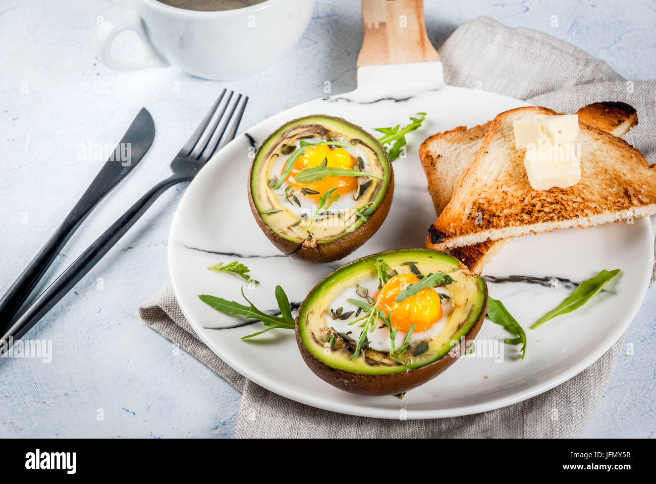 Gesunde vegane Frühstück. Ernährung. Gebackene Avocado mit Ei und frischem Salat aus Rucola, Toast und Butter. Auf eine weiße Marmorplatte, einem konkreten Leuchttisch. Stockfoto